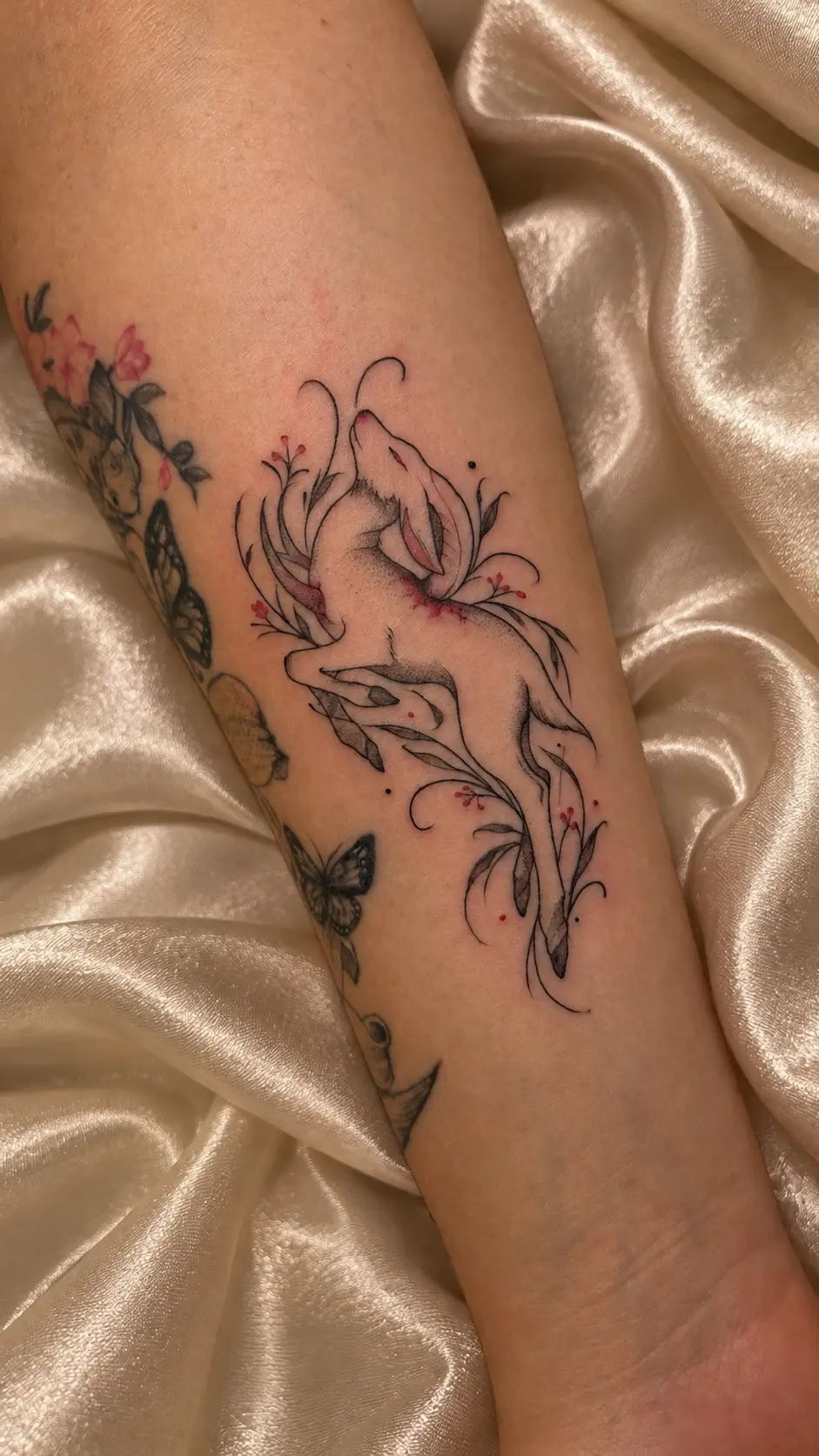 Tatuagem fine line de cordeiro saltando entre ramos, folhas e frutos vermelhos no antebraço